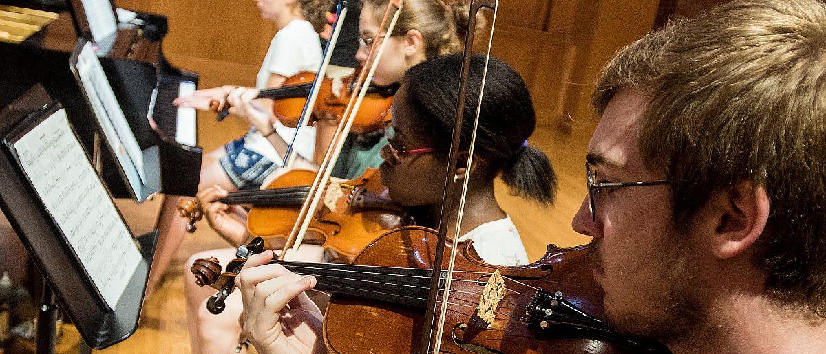 Image of students reading sheet music and playing violins.